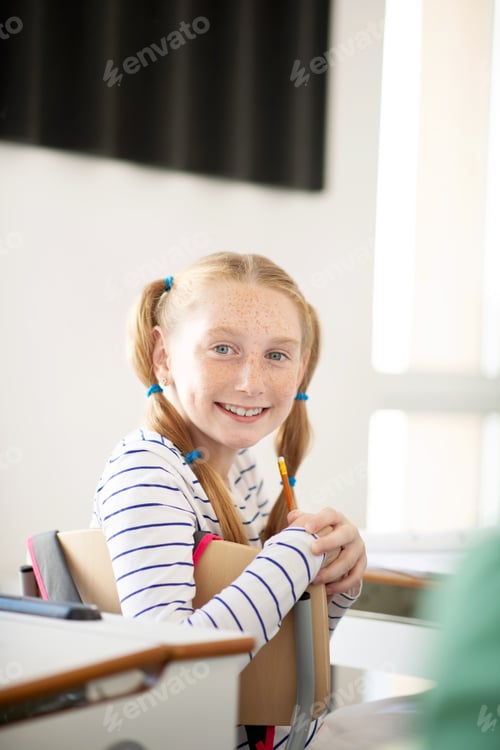 Visualização: Linda estudante vestindo camisa listrada sentada na mesa
