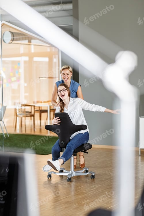 Preview: Playful employee pushing colleague on office chair