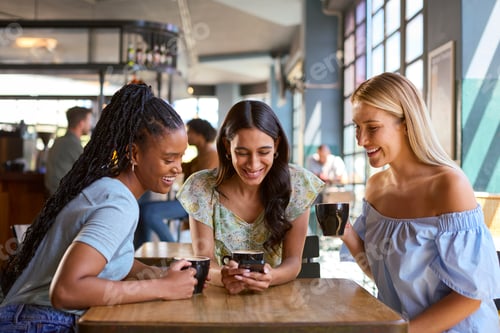 Preview: Group Of Female Friends Meeting Up In Restaurant Or Coffee Shop Looking At Mobile Phone