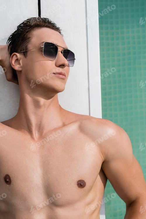 Preview: top view of shirtless man in sunglasses lying at poolside with hand behind head