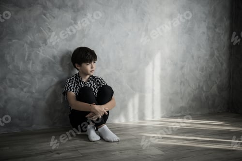 Preview: Sad boy sitting thinking sitting on the floor of the room against the house wall.