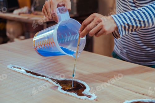 Preview: Closeup of carpenter pouring liquid epoxy in a wooden table
