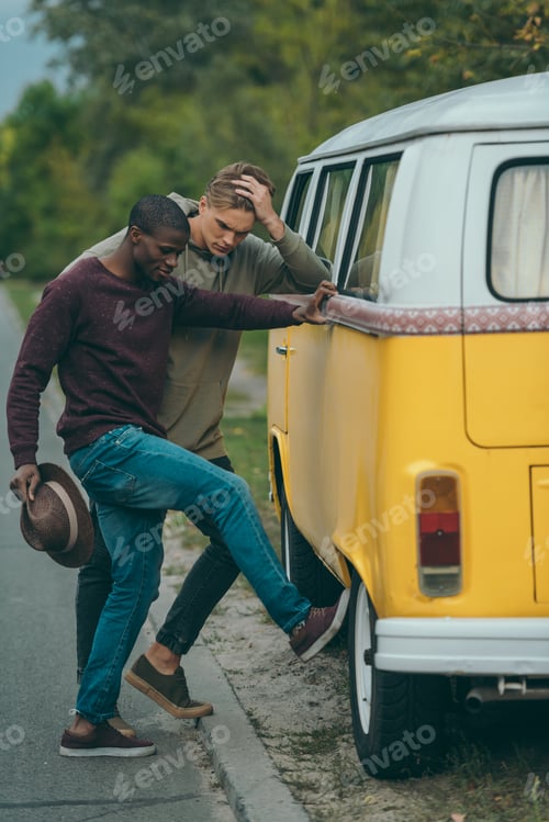Preview: upset multiethnic friends near broken minivan on road