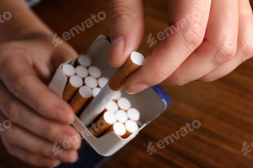 Preview: Woman taking cigarette out of pack at wooden table, closeup