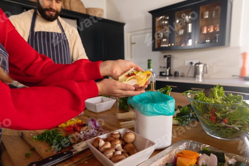 Preview: Happy caucasian couple preparing food in kitchen and composting vegetable scraps