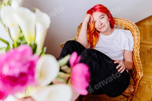 Preview: Young woman with red hair relaxing in a wicker chair at home