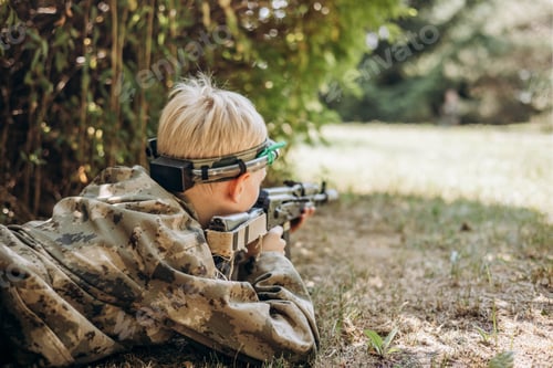 Preview: Teenager boy in camouflage with a weapon in his hand playing laser tag shooting game in outdoors