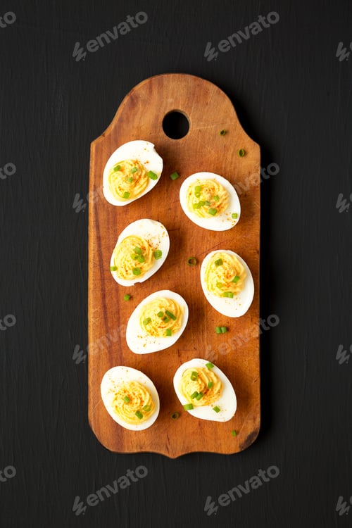 Preview: Homemade Deviled Eggs with Chives on a rustic wooden board on a black background, top view.