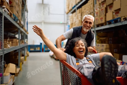 Preview: Happy warehouse worker having fun while being pushed in a cart by her coworker.