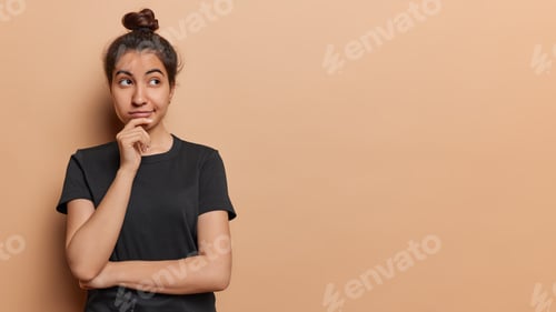Preview: Horizontal shot of lovely pensive Iranian girl keeps hand on chin concentrated asie has thoughtful