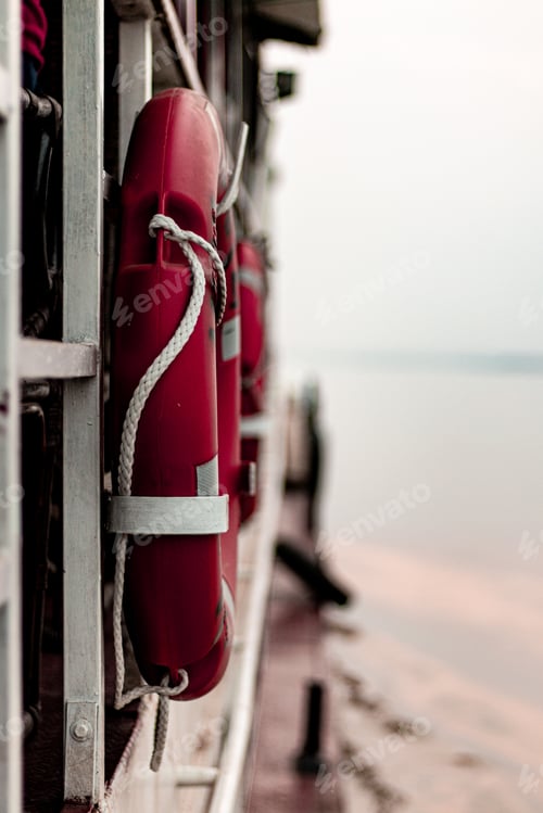 Preview: Vertical shot of a red lifebuoy ring attached with white ropes