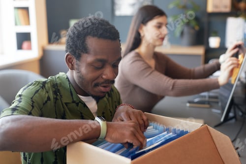 Preview: Smiling Black Man Looking Through Documents in Folder Box at Office