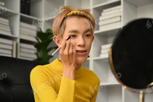 Preview: Teenage asian man applying eyeshadow powder in front of mirror.