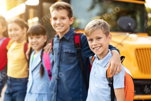 Preview: Happy multiethnic group of kids posing outside by yellow school bus