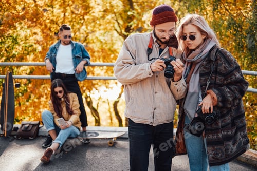 Preview: Company of friends relaxing and photographing in autumn park