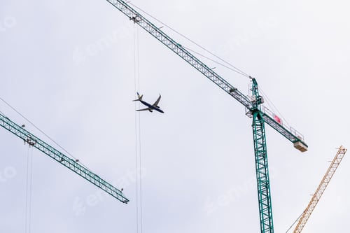 Preview: Plane flies over the city framed among building construction cranes, cities grow with tourism.