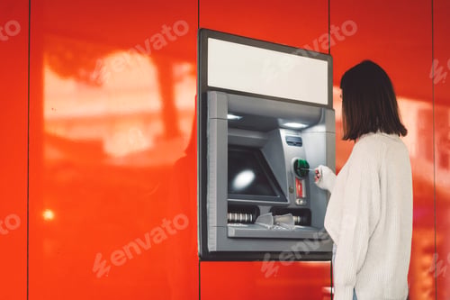 Preview: Side view of a woman inserting a card in the ATM on a red wall
