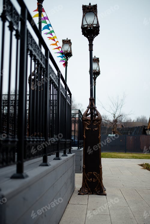 Preview: Metal black railings, bronze poles with lanterns and multicolored flags at the entrance to the fair.