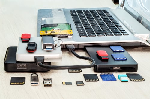 Preview: Stack of USB flash drives, memory cards, external hard drives in front, laptop