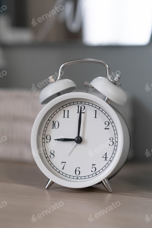 Preview: Close-up of a round white alarm clock on a table in the bedroom.