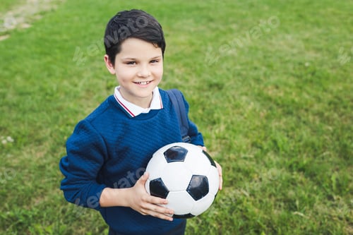 Preview: happy kid holding soccer ball and looking at camera on grass field
