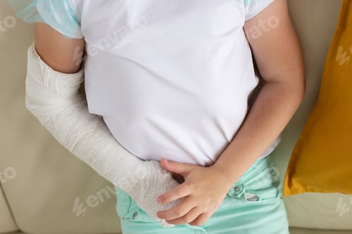 Preview: Close-up child girl with a cast on a broken wrist or arm smiling at home