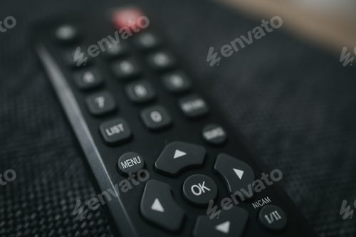 Preview: Closeup shot of a black portable remote control on a wooden table, menu and OK buttons