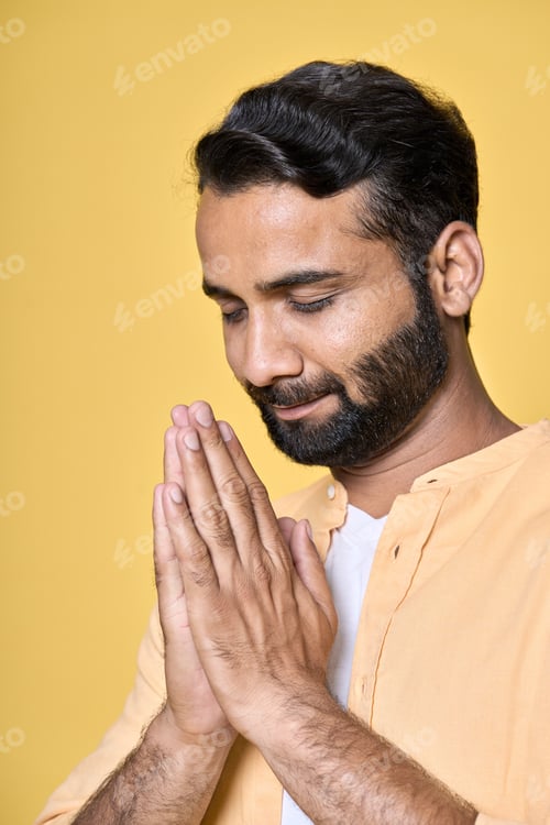 Preview: Mindful indian man meditating holding hands in namaste isolated on yellow.