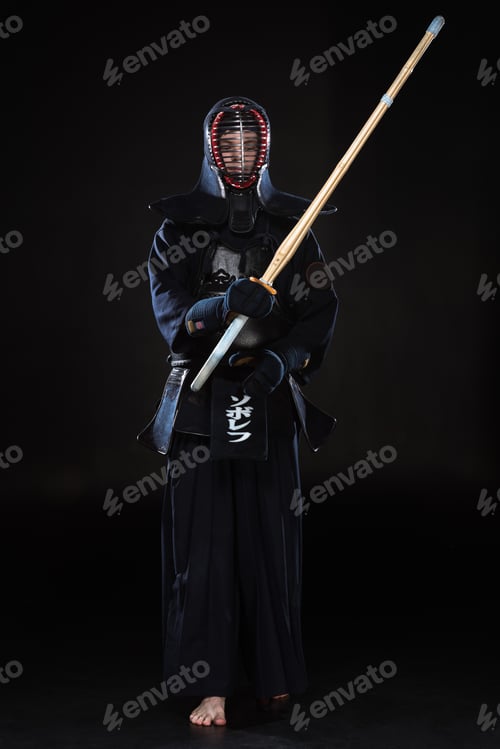 Preview: Full length view of kendo fighter in helmet holding bamboo sword on black