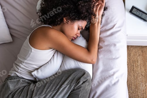 Preview: Top view of depressed and sad African American woman lying on the bed crying while hugging pillow.