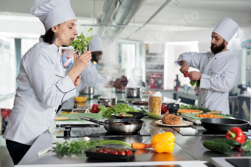 Preview: Head cook smelling fresh green herbs while sous chef cutting organic vegetables for gourmet cuisine