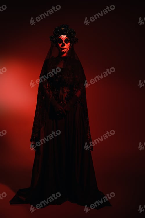 Preview: Full length of woman in mexican santa muerte costume looking at camera on burgundy background with