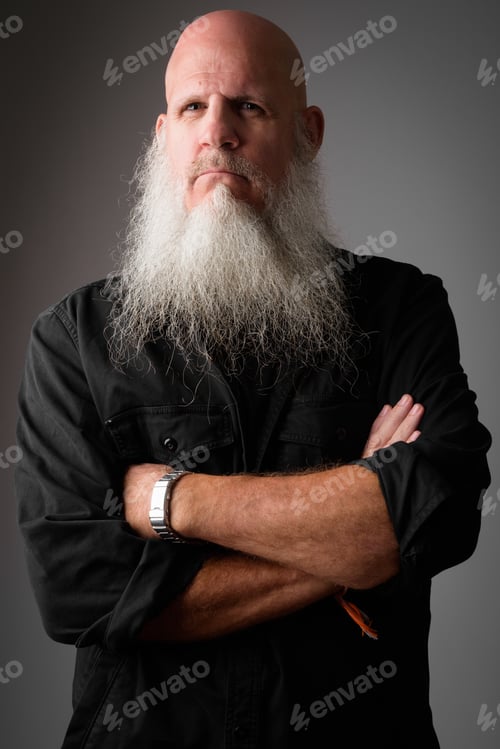 Preview: Studio shot of mature bald bearded man looking serious with arms crossed