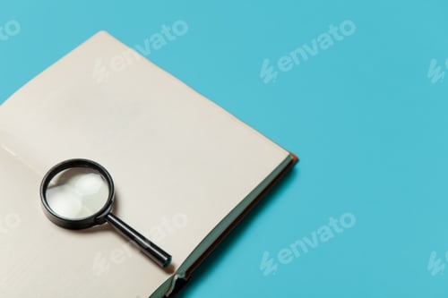 Preview: Opened book and loupe on color background.