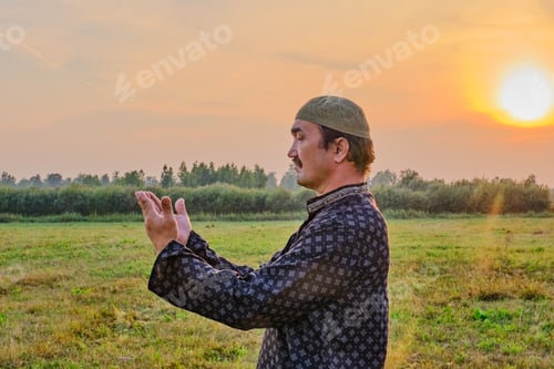 Preview: A Muslim senior man wearing a skullcap and traditional clothes prays at sunset