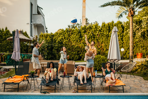 Preview: Friends playing with inflatable ball by the swimming pool at summer party