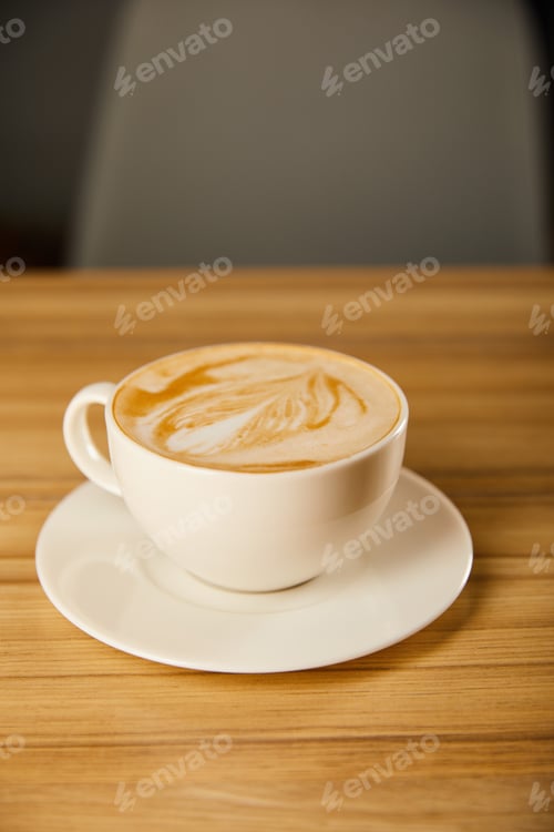 Preview: tasty cappuccino in white cup with saucer on table