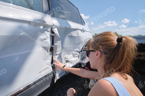 Preview: Sad female driver sitting on street side shocked after car accident.