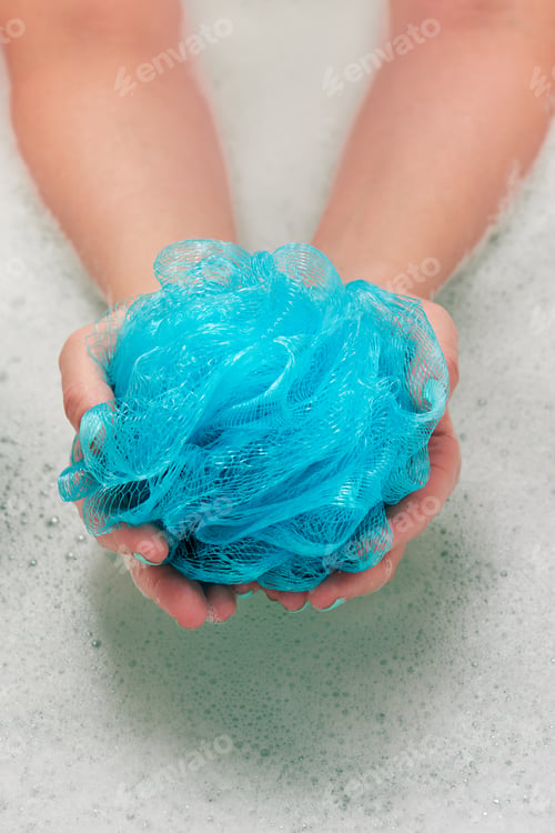Preview: female hands holding a round soft synthetic washcloth in bath with water. Hands close-up. Spa