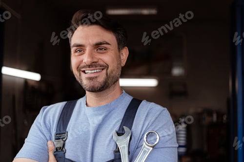 Preview: Mechanic smiles while holding tools in workshop during daytime hours
