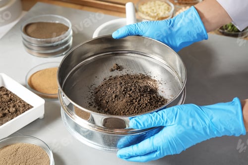 Preview: Scientist pulverizing and sieving soil samples at table, closeup. Laboratory analysis