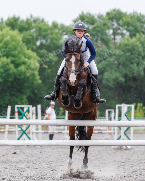 Preview: Young woman riding horseback jumping over the hurdle on showjumping course