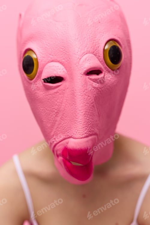 Preview: A woman wearing a silicone Halloween mask in the shape of a pink fish with big yellow eyes looks at