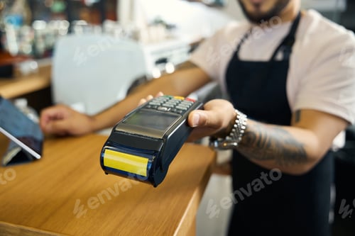 Preview: Young tattooed barista extending hand with a payment terminal