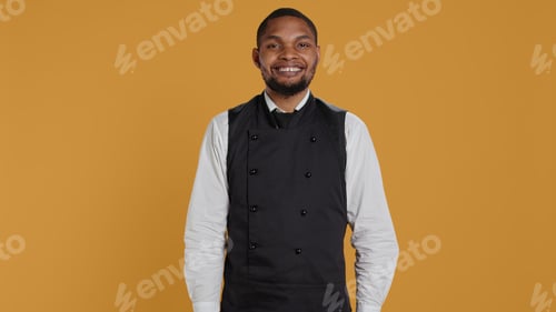 Preview: Waiter in apron and uniform showing a heart shape sign in studio