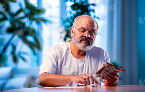 Preview: Elderly Indian man manages budget by counting cash and noting expenses at home