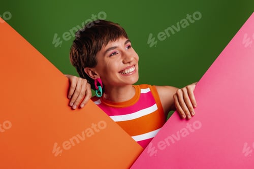 Preview: Happy young woman looking out of the colorful banners while standing against background