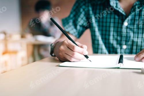 Preview: Close up of student hand writing on paper with a pencil in classroom.