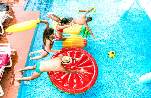 Preview: High angle view of millenial friends jumping at swimming pool party
