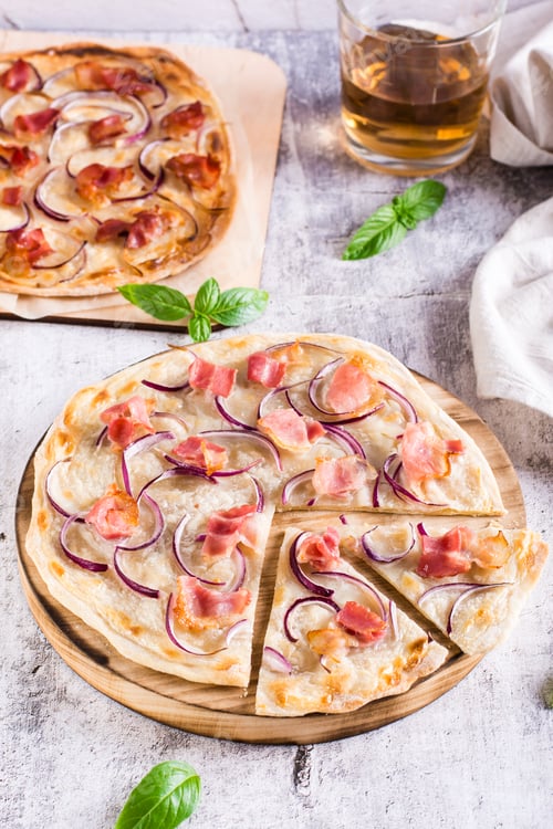 Preview: Traditional french flambee tart with cream cheese, bacon and onion on a board. Vertical view